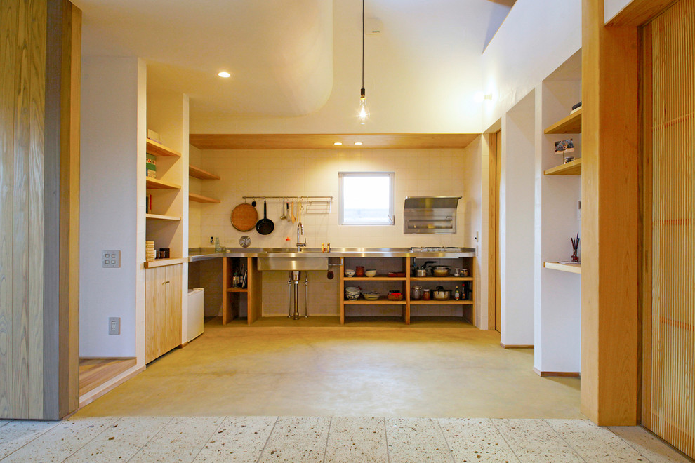 На фото: кухня-гостиная в восточном стиле с одинарной мойкой, открытыми фасадами, столешницей из нержавеющей стали, белым фартуком и коричневым полом