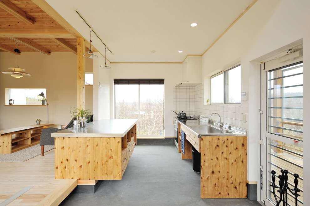 Galley concrete floor and gray floor open concept kitchen photo in Other with stainless steel countertops, flat-panel cabinets, medium tone wood cabinets, white backsplash and an island