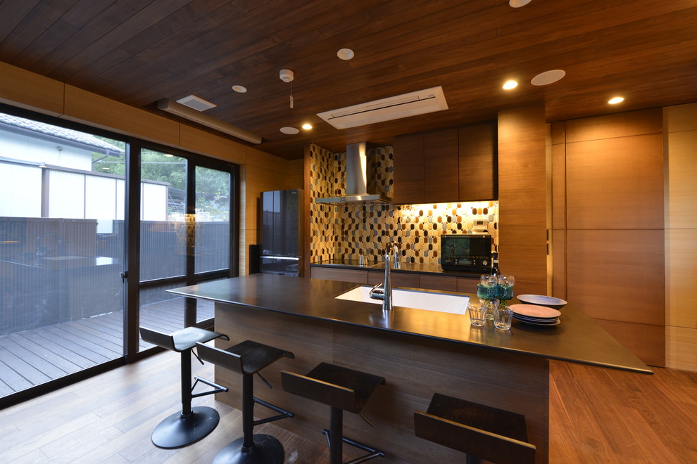 Inspiration pour une cuisine parallèle asiatique avec un évier 1 bac, un placard à porte plane, des portes de placard marrons, un sol en bois brun, îlot, un sol marron et plan de travail noir.