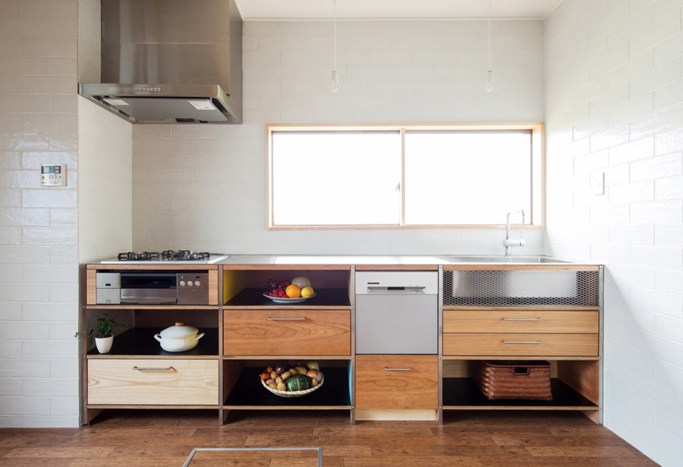 Einzeilige Moderne Küche mit flächenbündigen Schrankfronten, hellbraunen Holzschränken, Edelstahl-Arbeitsplatte, Küchenrückwand in Weiß, Küchengeräten aus Edelstahl und braunem Holzboden in Tokio