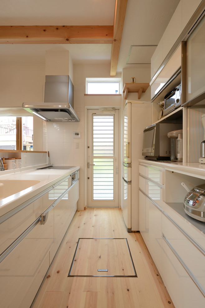 На фото: прямая кухня в стиле модернизм с монолитной мойкой, плоскими фасадами, белыми фасадами, светлым паркетным полом, полуостровом, бежевым полом и белой столешницей с