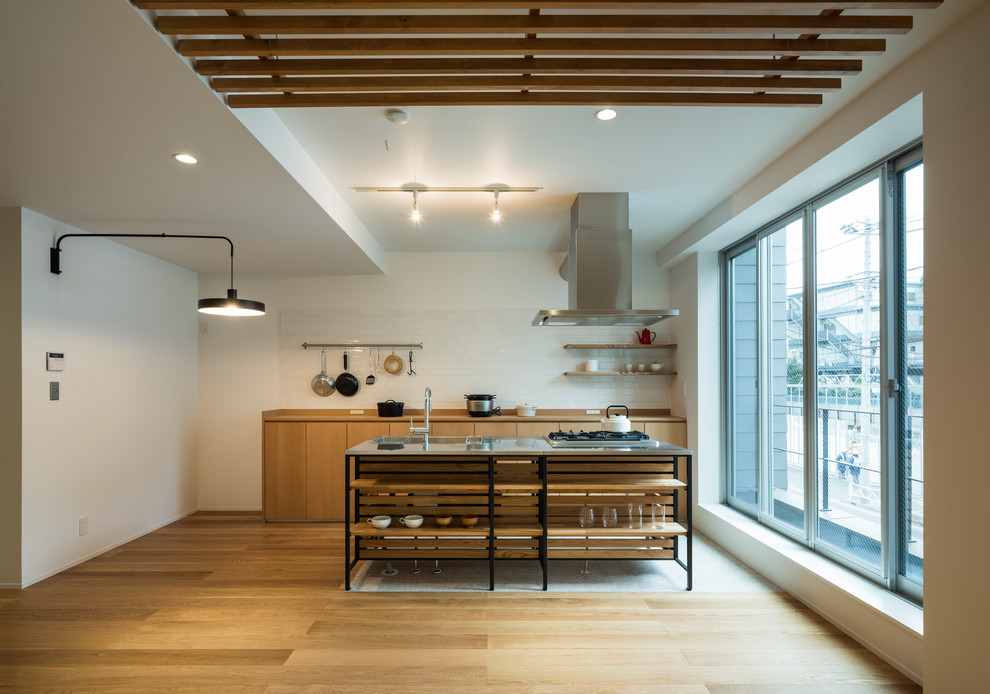 Zweizeilige Asiatische Küche mit flächenbündigen Schrankfronten, hellbraunen Holzschränken, Küchenrückwand in Weiß, Rückwand aus Metrofliesen, braunem Holzboden, Kücheninsel, braunem Boden und brauner Arbeitsplatte in Tokio