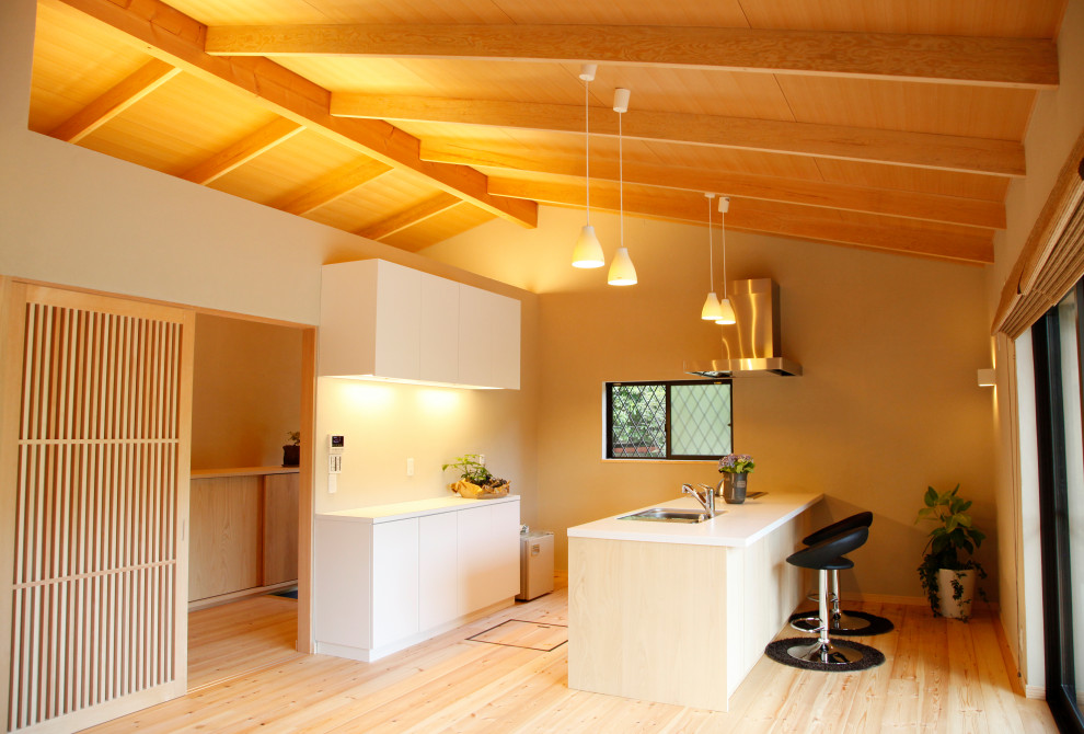 This is an example of a small scandinavian single-wall open plan kitchen in Kyoto with a submerged sink, flat-panel cabinets, white cabinets, composite countertops, light hardwood flooring, an island, white worktops and a vaulted ceiling.