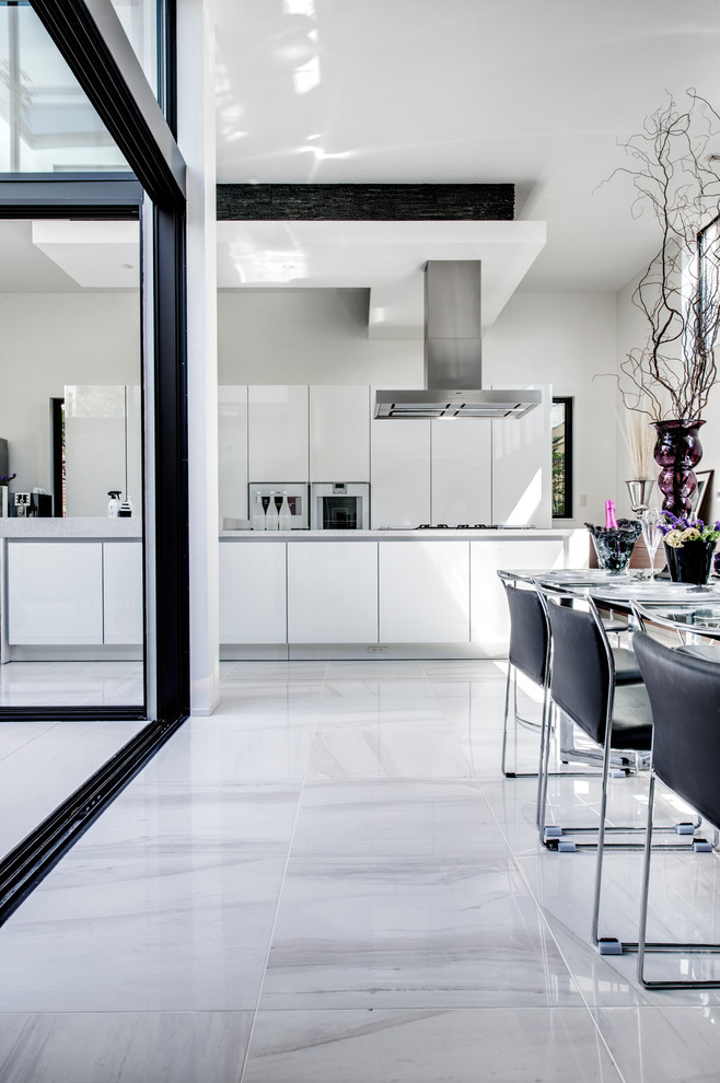 Foto på ett stort funkis linjärt kök med öppen planlösning, med en undermonterad diskho, släta luckor, vita skåp, rostfria vitvaror, marmorgolv och en köksö