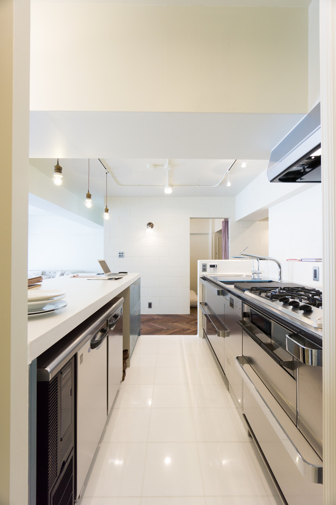 神戸にあるインダストリアルスタイルのおしゃれなキッチン (一体型シンク、白いキャビネット、人工大理石カウンター、白いキッチンパネル、磁器タイルのキッチンパネル、シルバーの調理設備、リノリウムの床、白い床) の写真