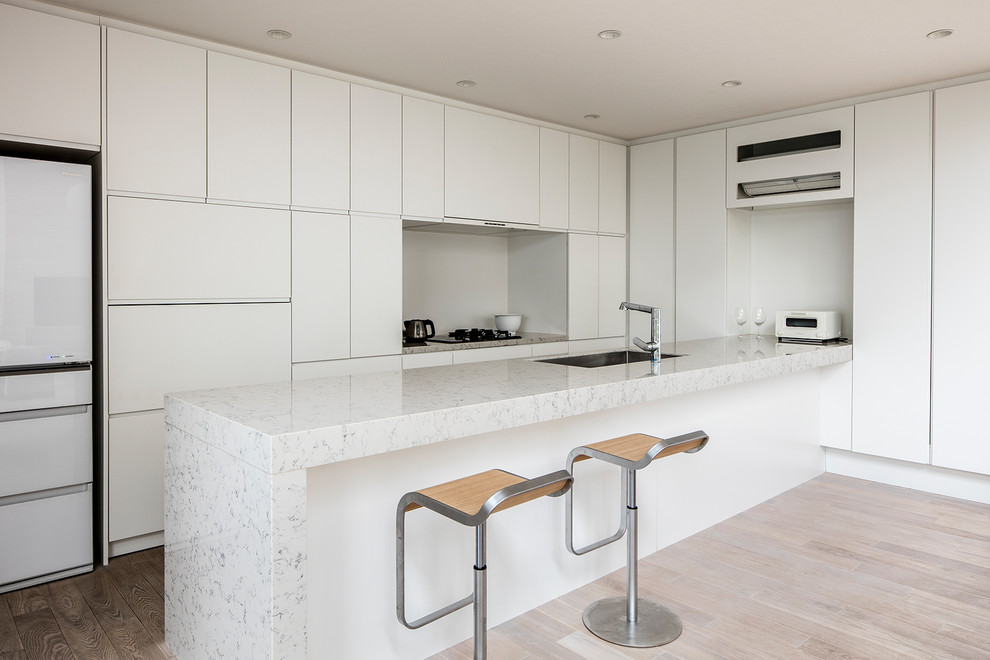 Inspiration for a modern galley open plan kitchen in Tokyo with a single-bowl sink, flat-panel cabinets, white cabinets, marble worktops, painted wood flooring, a breakfast bar, beige floors and white appliances.