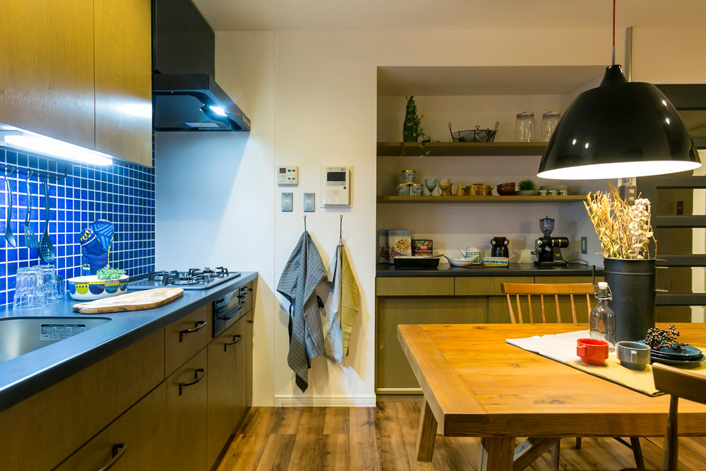 Réalisation d'une cuisine ouverte linéaire nordique en bois foncé avec un évier 1 bac, un placard à porte plane, une crédence bleue, parquet peint et un sol marron.