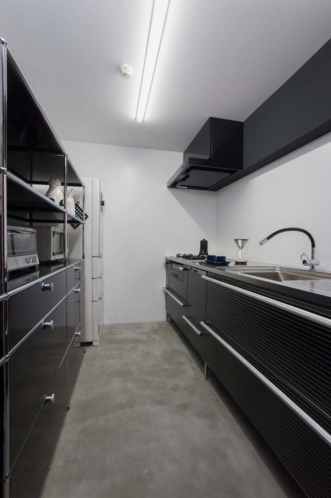 大阪にあるコンテンポラリースタイルのおしゃれなI型キッチン (アンダーカウンターシンク、フラットパネル扉のキャビネット、黒いキャビネット、ステンレスカウンター、白いキッチンパネル、黒い調理設備、コンクリートの床、アイランドなし) の写真
