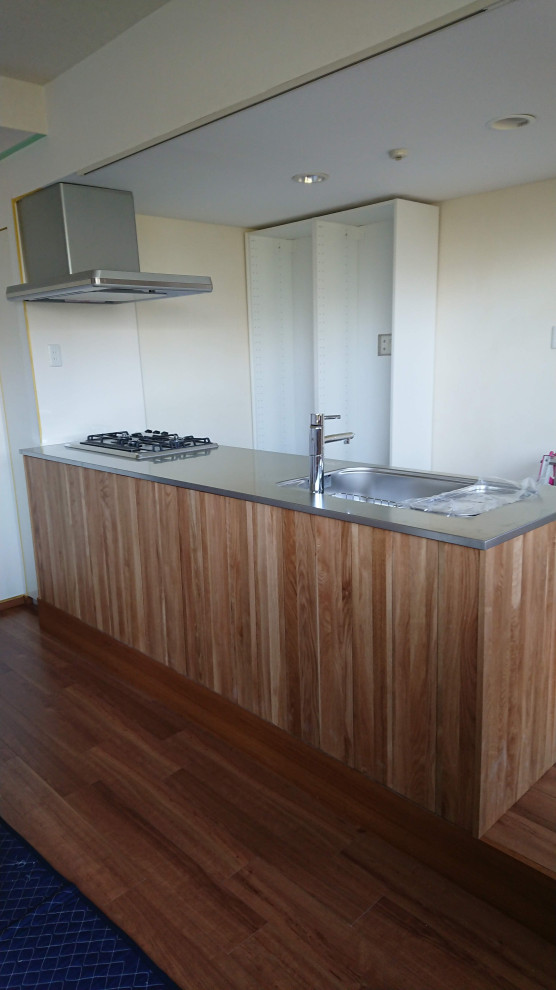 Large traditional single-wall open plan kitchen in Other with a single-bowl sink, recessed-panel cabinets, light wood cabinets, stainless steel worktops, white splashback, slate splashback, stainless steel appliances, medium hardwood flooring, an island, brown floors and brown worktops.