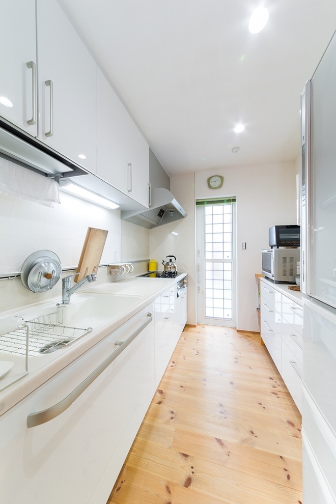 Imagen de cocina estrecha de estilo zen con fregadero integrado, puertas de armario blancas, salpicadero blanco, suelo de madera en tonos medios y suelo marrón