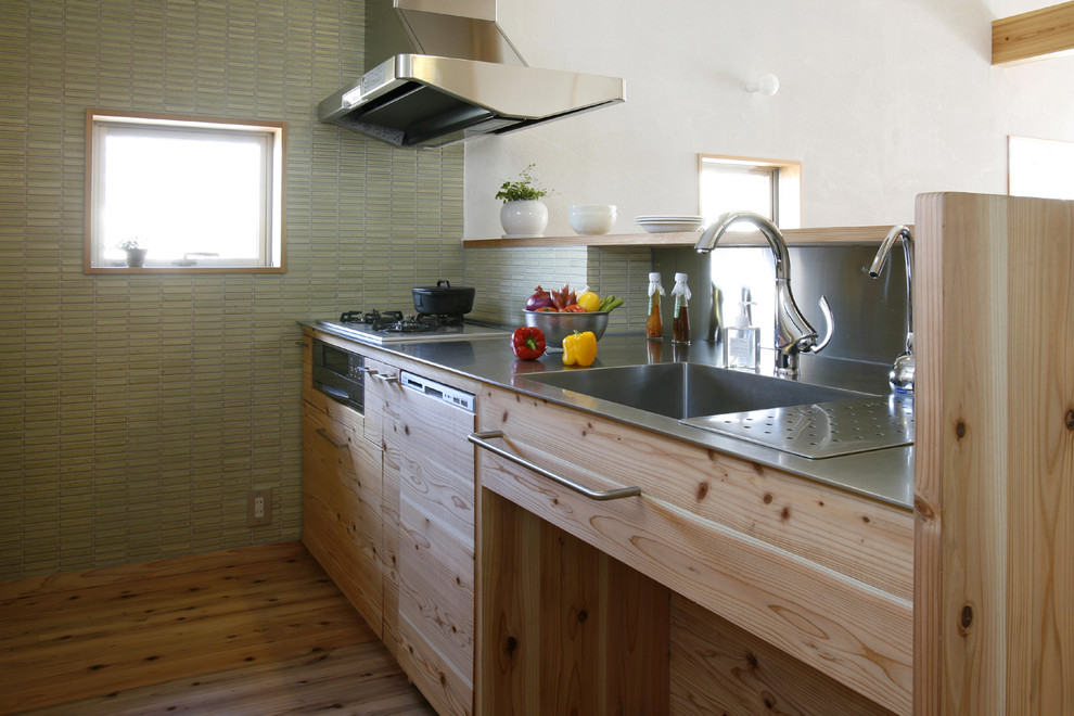 Idéer för att renovera ett mellanstort funkis linjärt kök med öppen planlösning, med en integrerad diskho, skåp i ljust trä, bänkskiva i rostfritt stål, grönt stänkskydd, rostfria vitvaror, stänkskydd i porslinskakel, mellanmörkt trägolv, en köksö och brunt golv