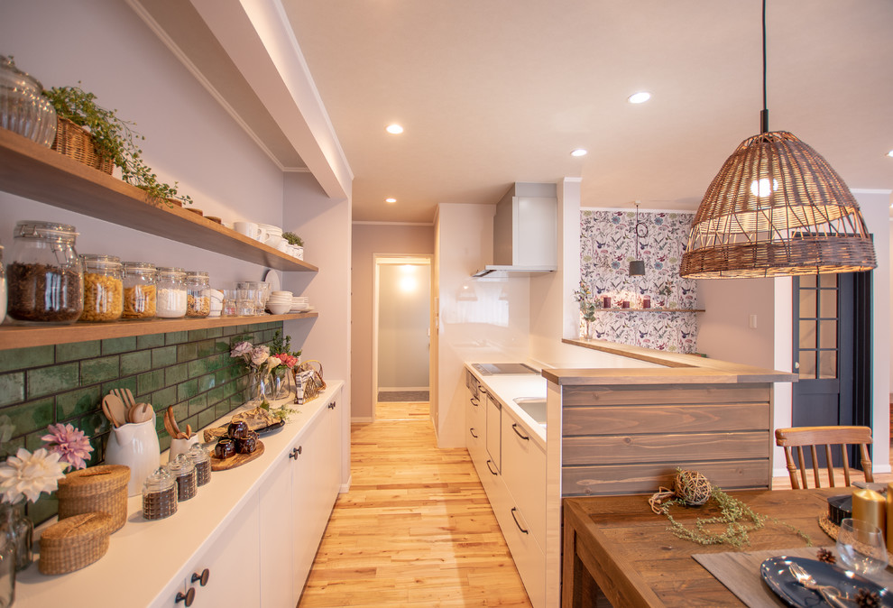 This is an example of a country single-wall open plan kitchen in Other with a single-bowl sink, flat-panel cabinets, white cabinets, medium hardwood flooring, a breakfast bar, brown floors, white splashback and white worktops.