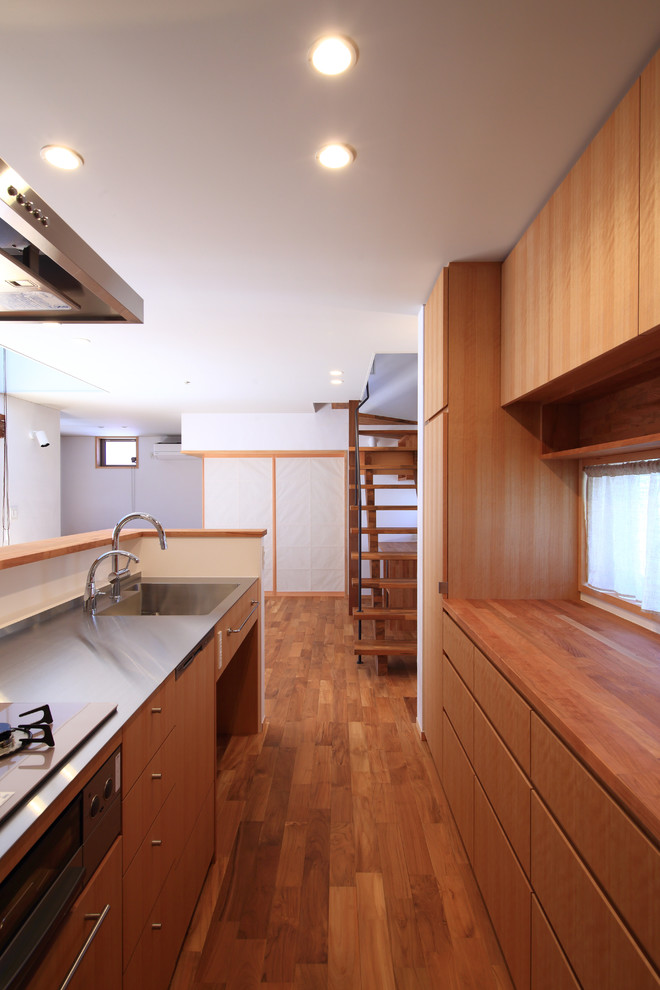 名古屋にある北欧スタイルのおしゃれなキッチン (一体型シンク、フラットパネル扉のキャビネット、茶色いキャビネット、ステンレスカウンター、白いキッチンパネル、シルバーの調理設備、濃色無垢フローリング、茶色い床、グレーのキッチンカウンター) の写真