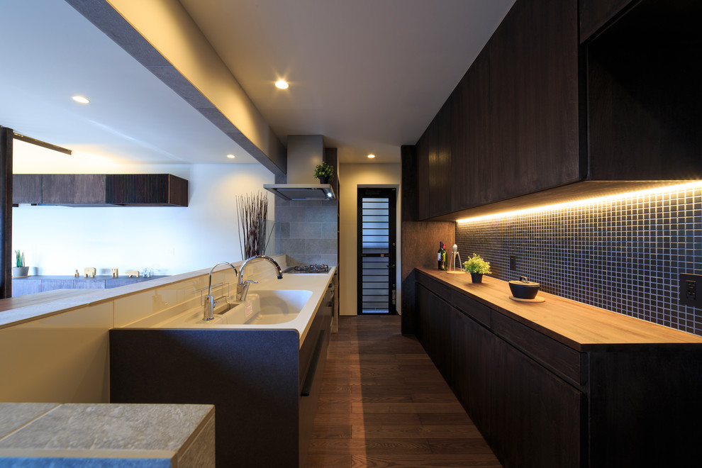 This is an example of a world-inspired single-wall open plan kitchen in Other with an integrated sink, flat-panel cabinets, dark wood cabinets, white splashback, dark hardwood flooring, a breakfast bar, brown floors and brown worktops.