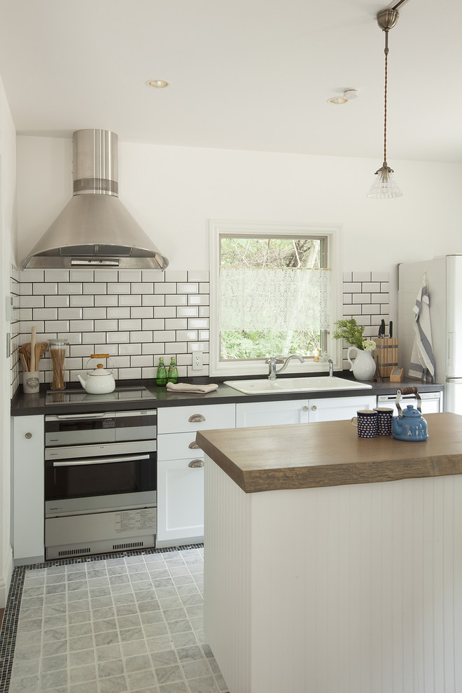 Lantlig inredning av ett linjärt kök och matrum, med en enkel diskho, klinkergolv i porslin, en köksö, grått golv, luckor med infälld panel, vita skåp och vitt stänkskydd