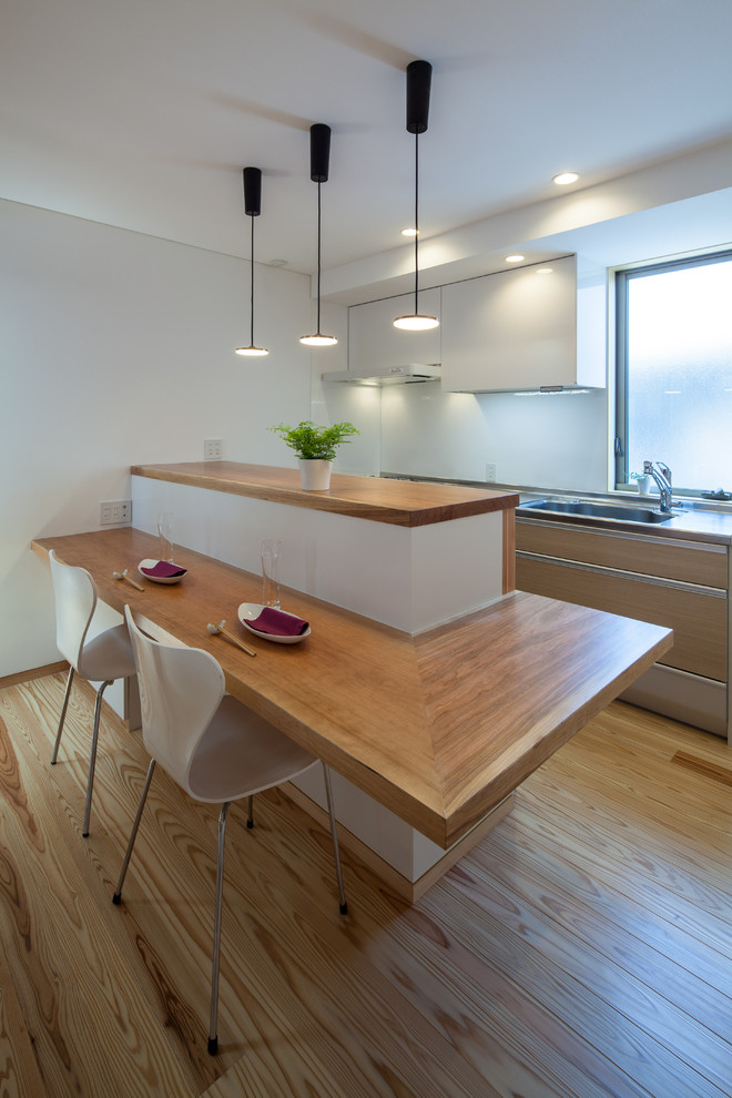Foto på ett funkis kök, med en undermonterad diskho, släta luckor, skåp i ljust trä, bänkskiva i rostfritt stål, vitt stänkskydd, rostfria vitvaror, ljust trägolv och en halv köksö