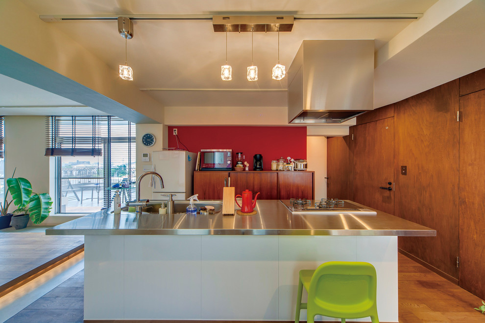 На фото: параллельная кухня-гостиная в стиле лофт с накладной мойкой, столешницей из нержавеющей стали, паркетным полом среднего тона и островом с