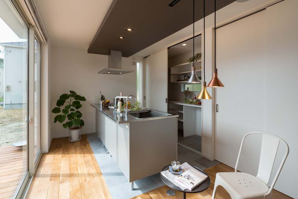 Idee per un piccolo cucina con isola centrale industriale con top in acciaio inossidabile e pavimento in legno massello medio