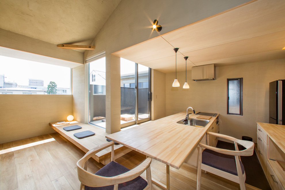 Cette photo montre une cuisine ouverte parallèle asiatique en bois clair avec un évier 1 bac, un placard à porte plane, un plan de travail en bois, parquet clair, une péninsule et un sol marron.