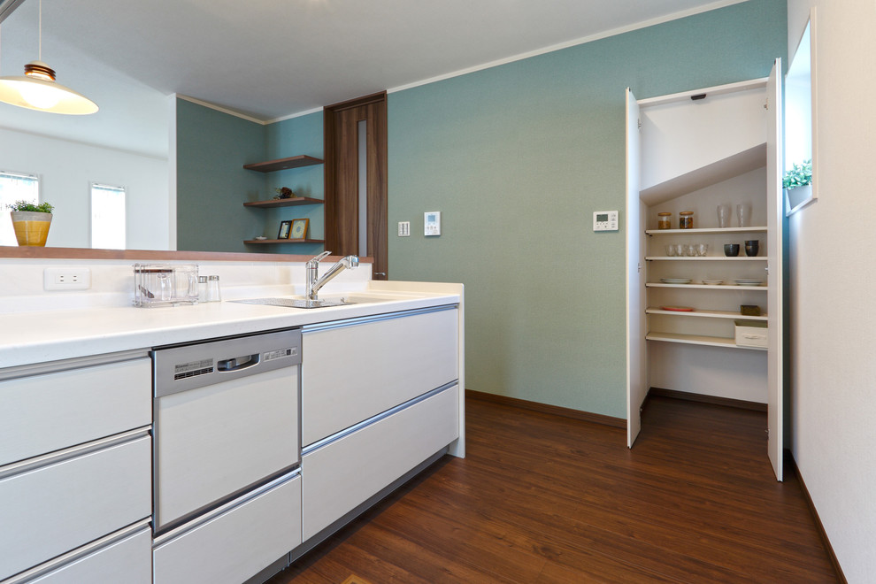 Immagine di un cucina con isola centrale minimal con lavello integrato, ante lisce, ante bianche, paraspruzzi bianco, pavimento in legno massello medio e pavimento marrone