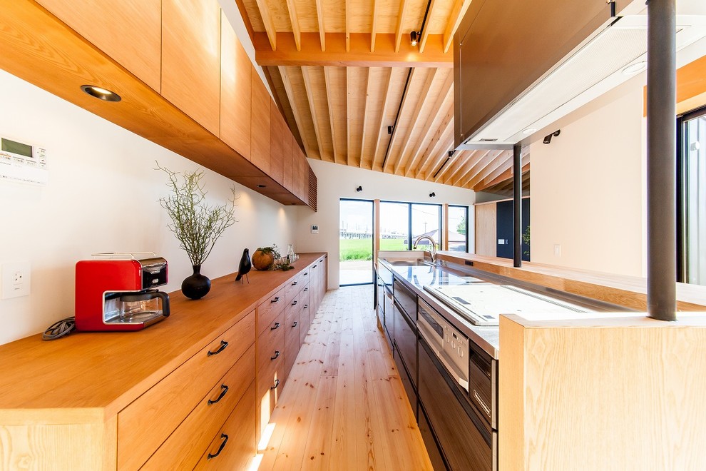 Idéer för att renovera ett orientaliskt brun linjärt brunt kök med öppen planlösning, med en integrerad diskho, släta luckor, bänkskiva i rostfritt stål, ljust trägolv, en köksö och brunt golv