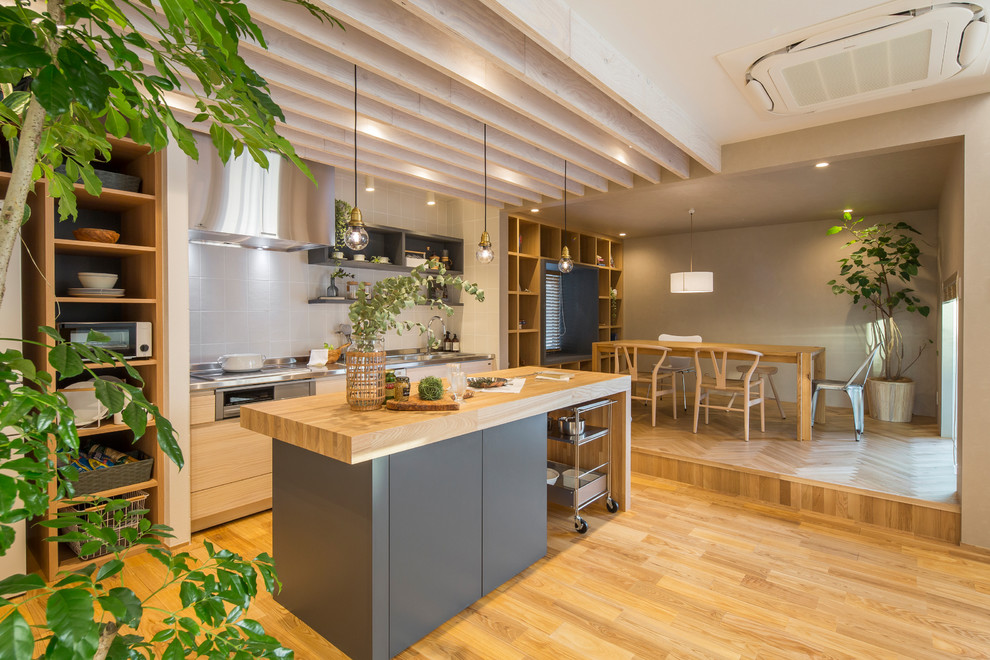 Einzeilige Moderne Wohnküche mit flächenbündigen Schrankfronten, grauen Schränken, Edelstahl-Arbeitsplatte, Küchenrückwand in Grau, hellem Holzboden, Kücheninsel und braunem Boden in Nagoya