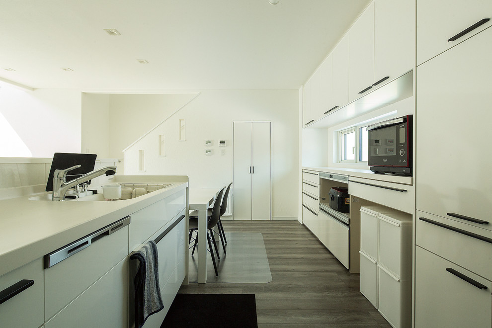 他の地域にあるコンテンポラリースタイルのおしゃれなアイランドキッチン (一体型シンク、フラットパネル扉のキャビネット、白いキャビネット、白いキッチンパネル、グレーの床) の写真