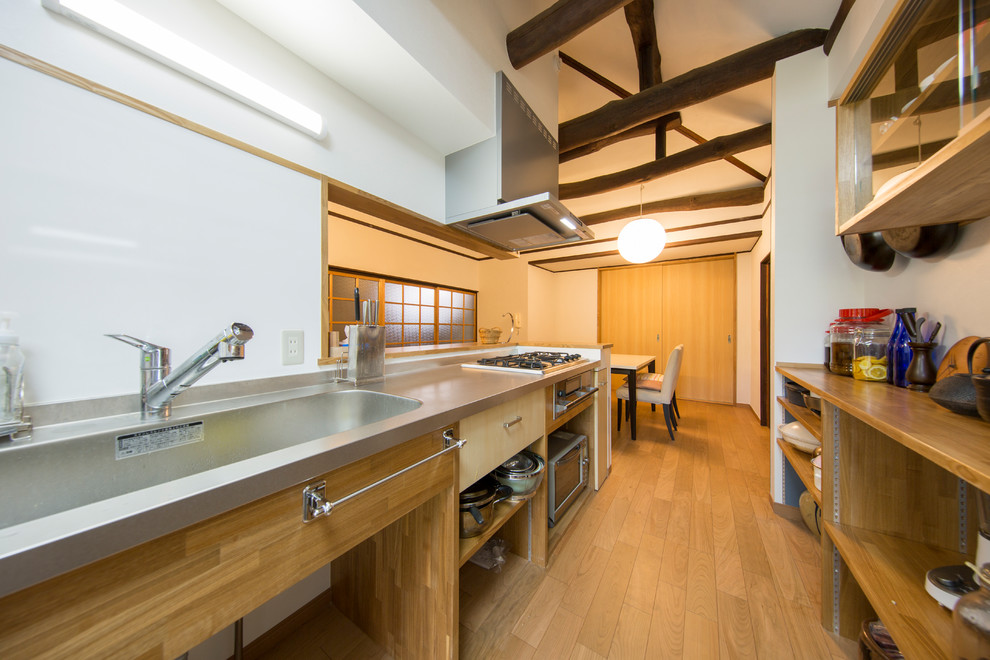 他の地域にあるアジアンスタイルのおしゃれなキッチン (シングルシンク、オープンシェルフ、ステンレスカウンター、白いキッチンパネル、無垢フローリング、茶色い床) の写真