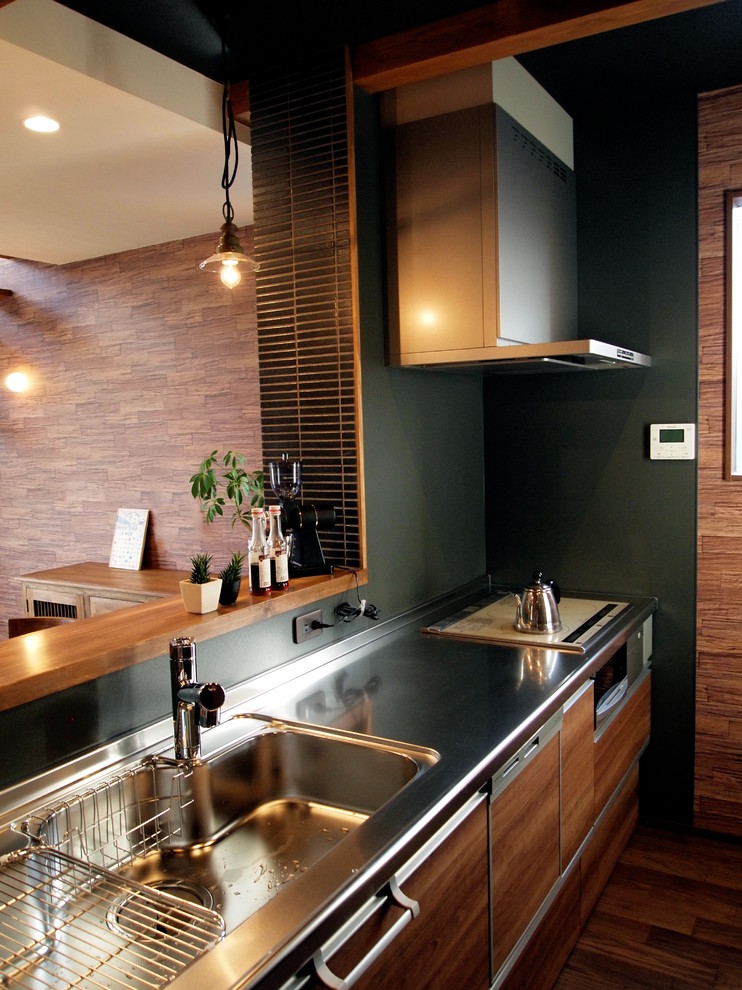 Idée de décoration pour une cuisine asiatique avec un placard à porte plane, des portes de placard marrons, un plan de travail en inox, une crédence verte, un sol en bois brun et un sol marron.