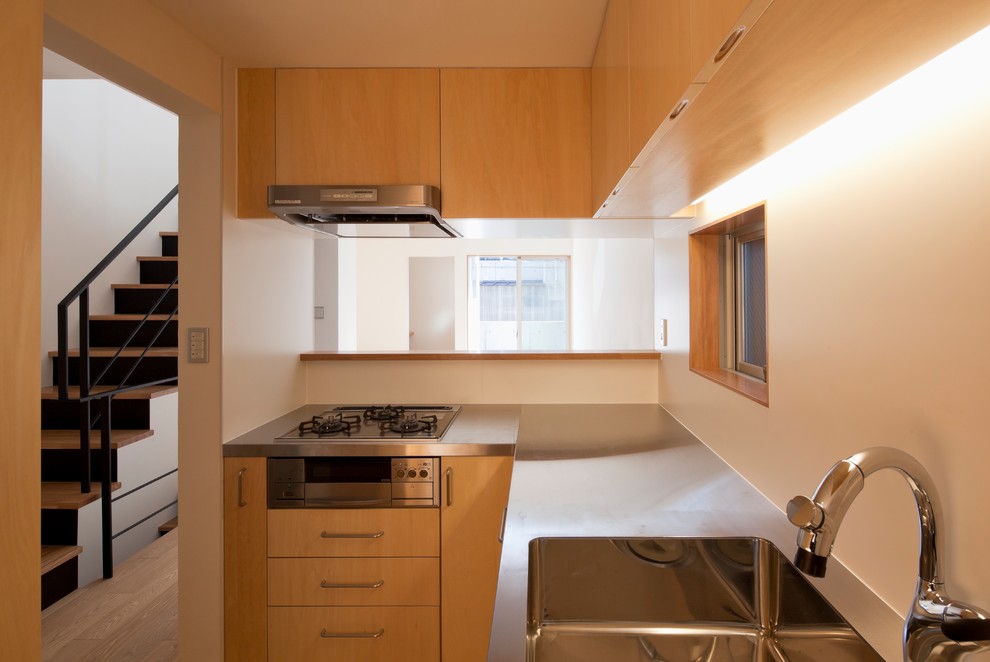 Example of a small l-shaped plywood floor and brown floor enclosed kitchen design in Tokyo with an integrated sink, flat-panel cabinets, medium tone wood cabinets, stainless steel countertops, white backsplash, black appliances and an island