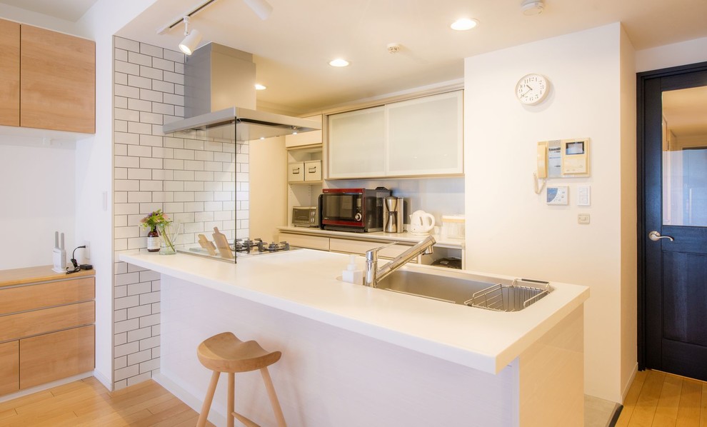 Foto på ett minimalistiskt kök, med en enkel diskho, släta luckor, vita skåp, en halv köksö och beiget golv