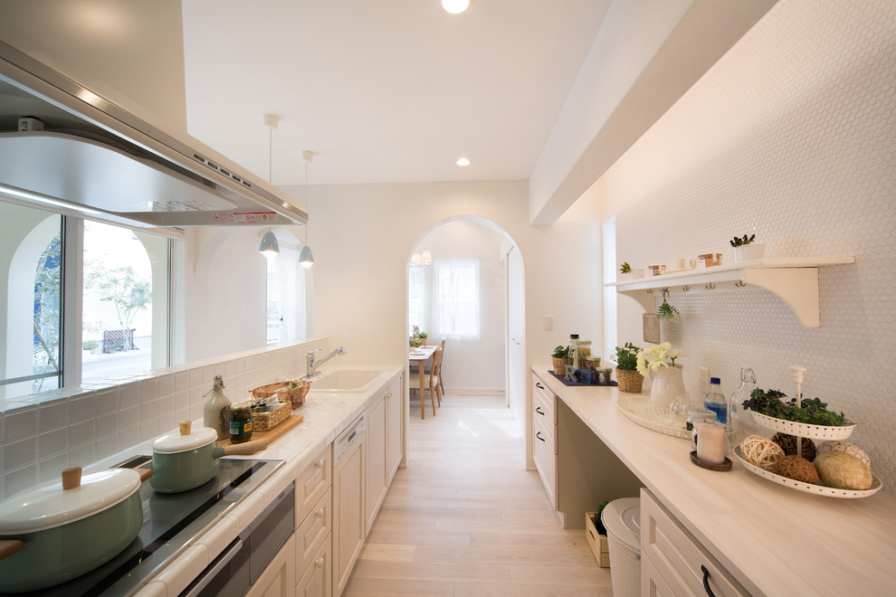 Foto de cocina alargada mediterránea con fregadero encastrado, armarios con paneles con relieve, puertas de armario blancas, suelo de madera pintada y una isla