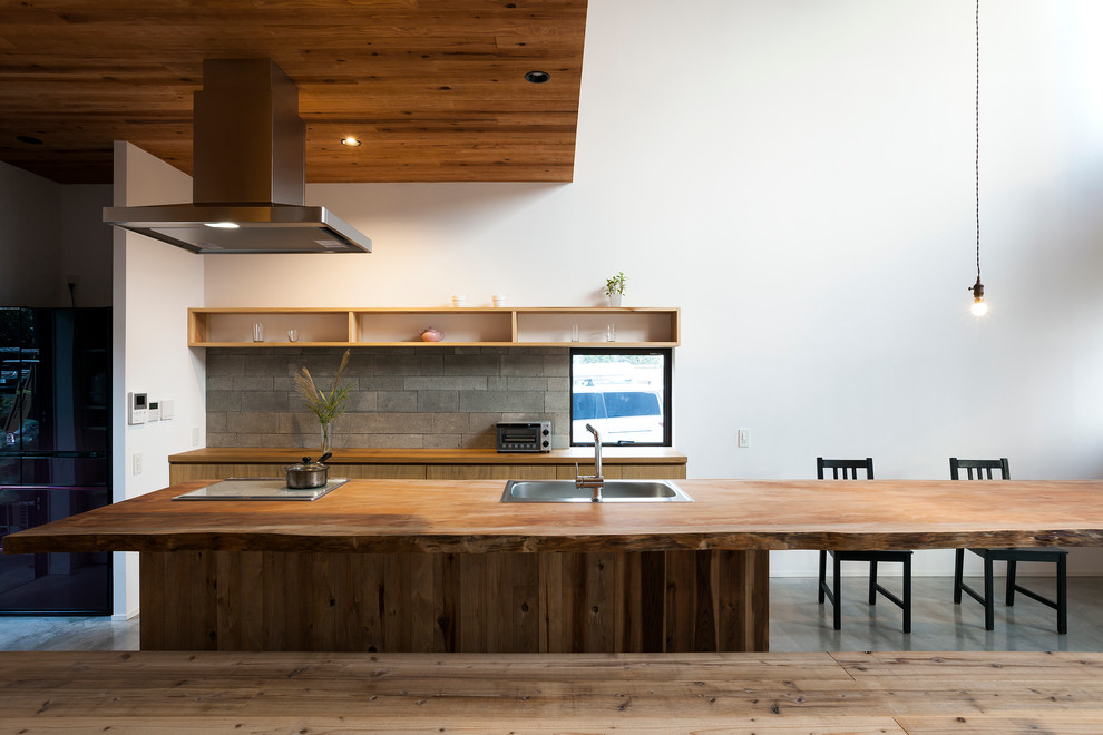 На фото: прямая кухня в восточном стиле с фасадами цвета дерева среднего тона, деревянной столешницей, светлым паркетным полом, островом, обеденным столом и одинарной мойкой с