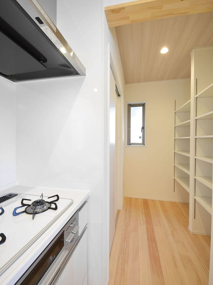 Réalisation d'une cuisine ouverte linéaire asiatique avec un placard sans porte, des portes de placard blanches, une crédence blanche, un sol beige et un plan de travail blanc.