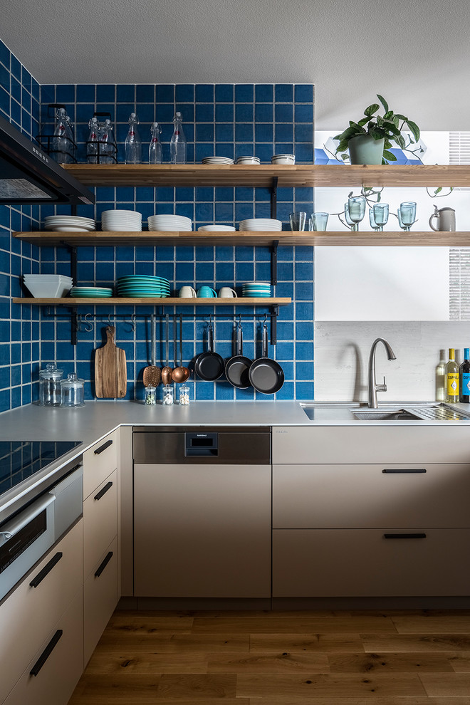 Design ideas for a modern l-shaped open plan kitchen in Tokyo with a submerged sink, beaded cabinets, grey cabinets, blue splashback, black appliances, medium hardwood flooring, a breakfast bar, brown floors and grey worktops.