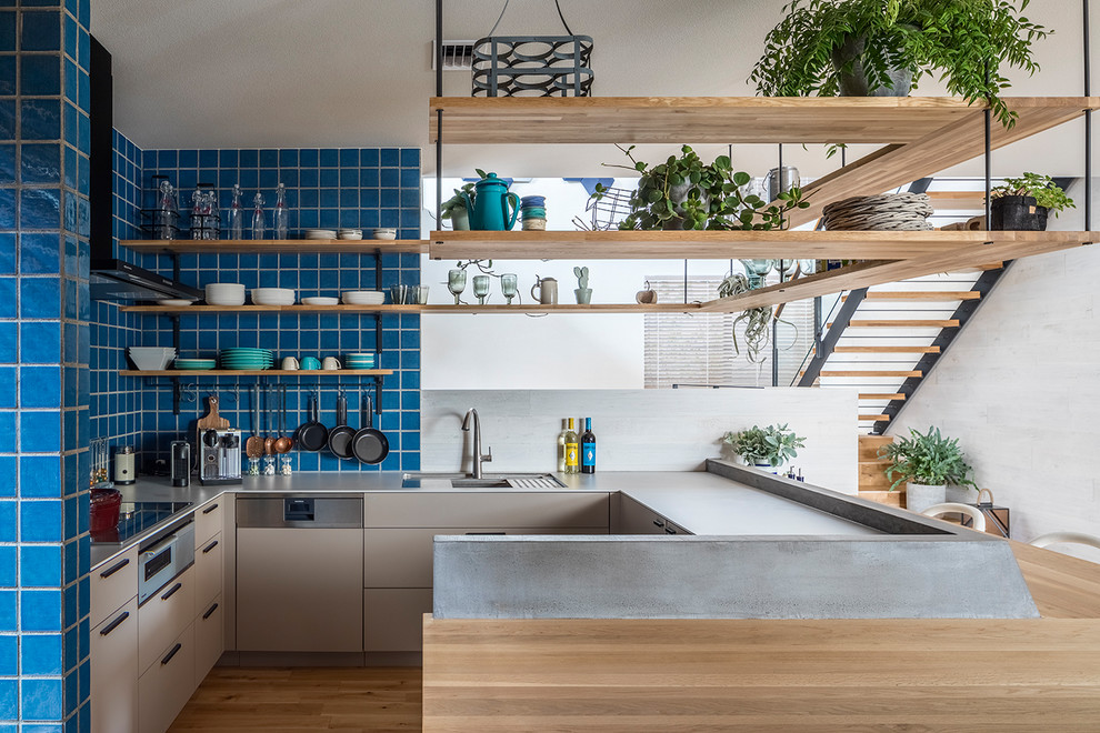 Photo of a modern l-shaped open plan kitchen in Tokyo with a submerged sink, beaded cabinets, grey cabinets, blue splashback, black appliances, medium hardwood flooring, a breakfast bar, brown floors and grey worktops.