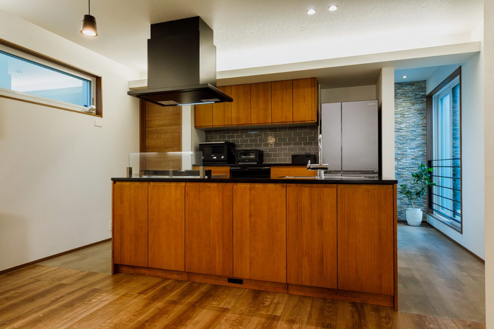 Стильный дизайн: кухня-гостиная среднего размера, у окна в современном стиле с плоскими фасадами, коричневыми фасадами, паркетным полом среднего тона, островом, коричневым полом, потолком с обоями, врезной мойкой и черной техникой - последний тренд