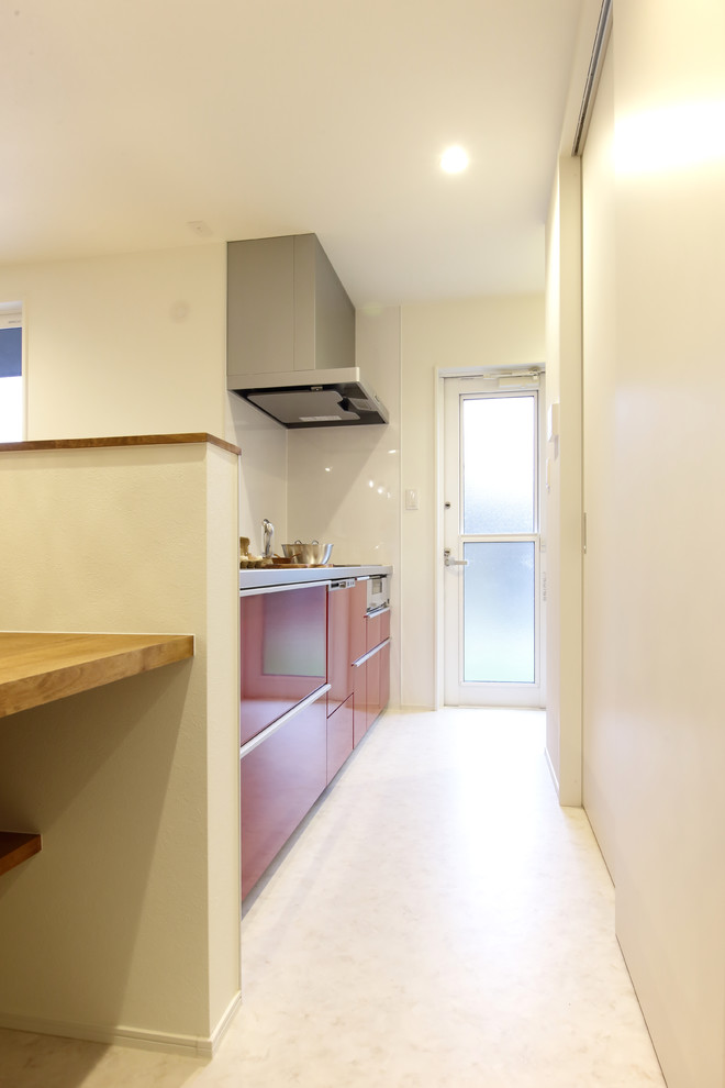 This is an example of a small modern single-wall open plan kitchen in Other with red cabinets, stainless steel worktops, white splashback, vinyl flooring and white floors.