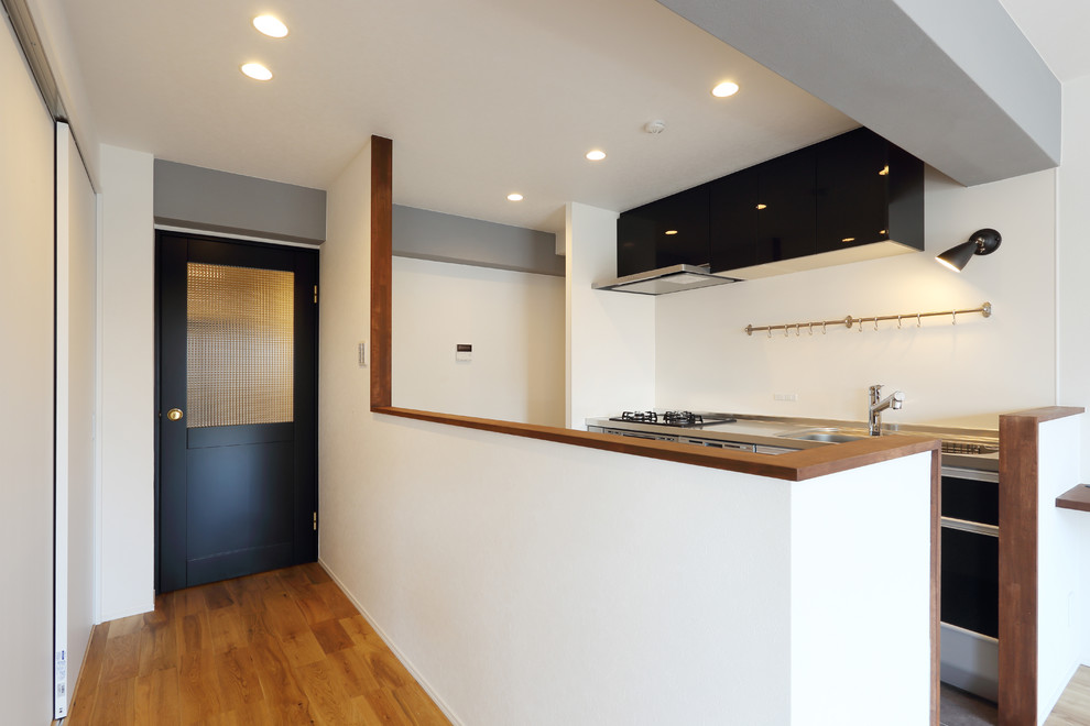 Inspiration pour une cuisine ouverte linéaire minimaliste de taille moyenne avec des portes de placard noires, une crédence blanche, parquet clair et un sol marron.