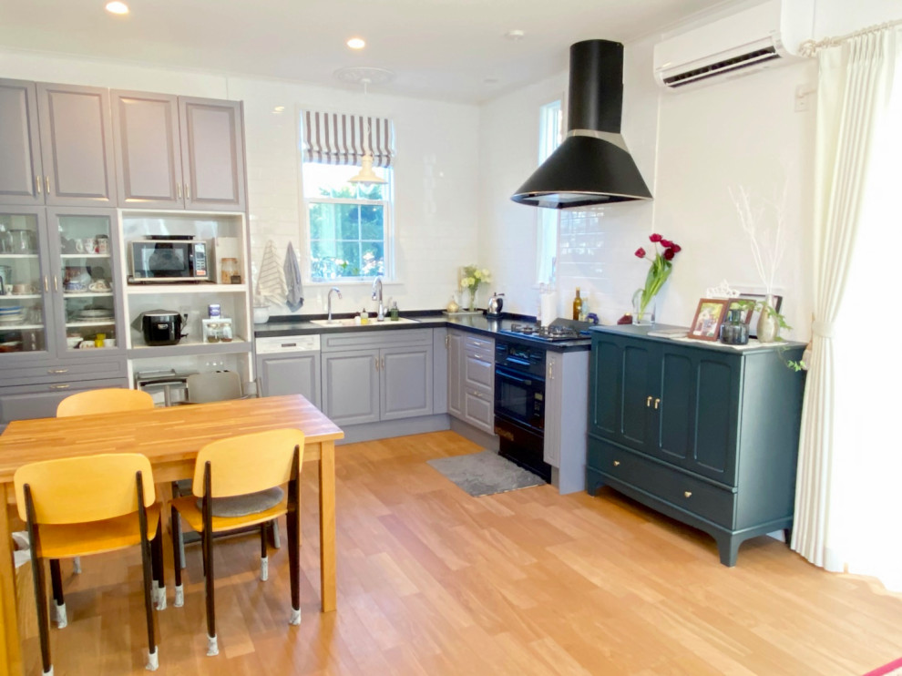 Mid-sized l-shaped plywood floor, brown floor and wallpaper ceiling open concept kitchen photo in Tokyo Suburbs with blue cabinets, white backsplash, porcelain backsplash, black appliances, no island and black countertops