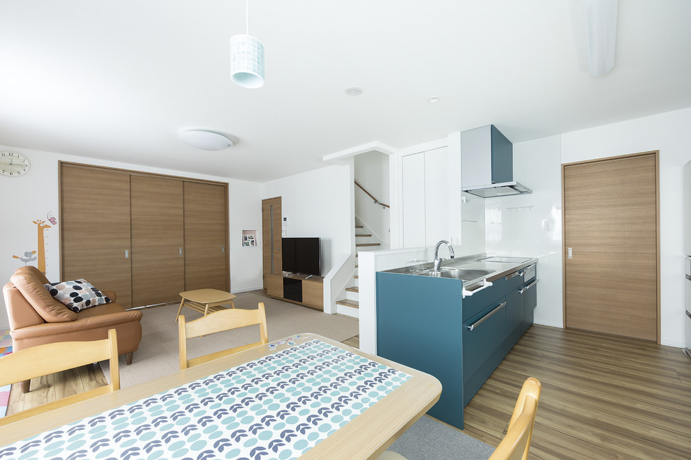 Scandinavian single-wall open plan kitchen in Other with a single-bowl sink, flat-panel cabinets, blue cabinets, stainless steel worktops, white splashback, painted wood flooring, an island and brown floors.