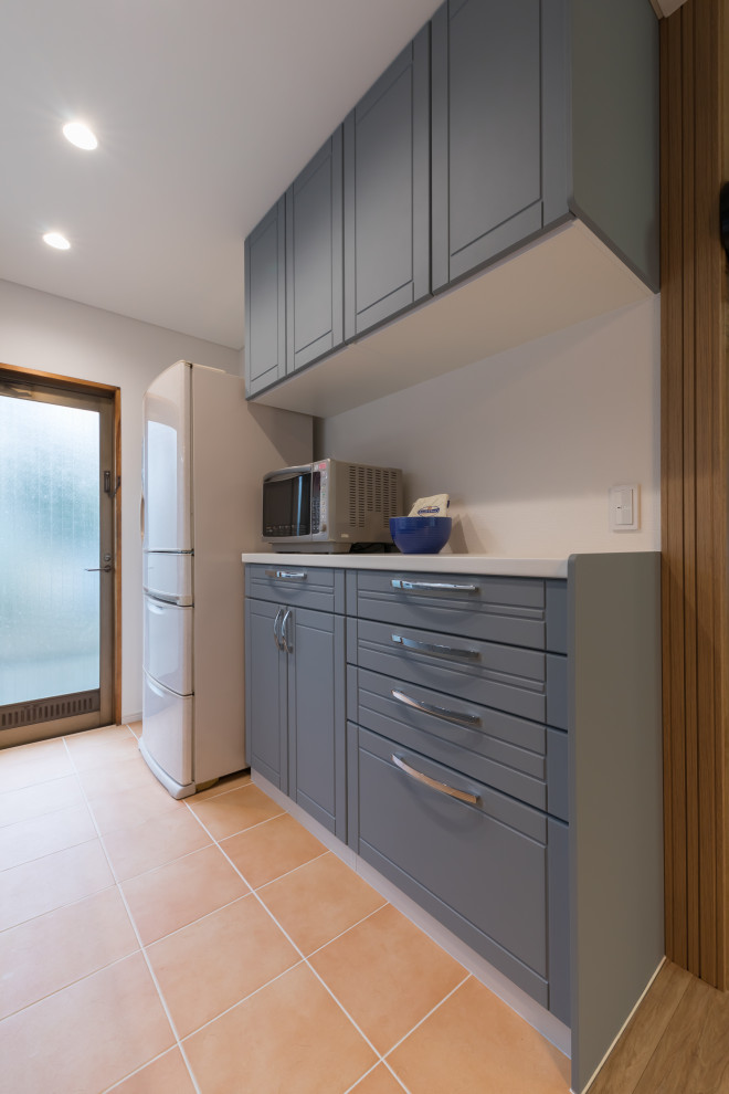 Cette image montre une petite cuisine ouverte linéaire nordique avec des portes de placard bleues, un plan de travail en surface solide, une crédence blanche, tomettes au sol, un sol orange, un plan de travail blanc et un plafond en papier peint.