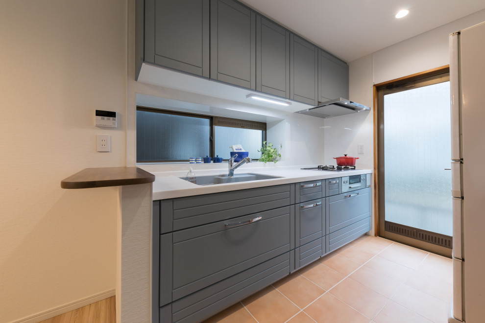 Cette image montre une petite cuisine ouverte linéaire nordique avec des portes de placard bleues, un plan de travail en surface solide, une crédence blanche, un plan de travail blanc, tomettes au sol, un sol orange et un plafond en papier peint.