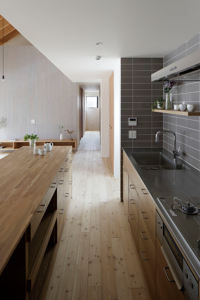 Foto på ett skandinaviskt brun kök med öppen planlösning, med en integrerad diskho, släta luckor, skåp i mellenmörkt trä, bänkskiva i rostfritt stål, ljust trägolv och beiget golv