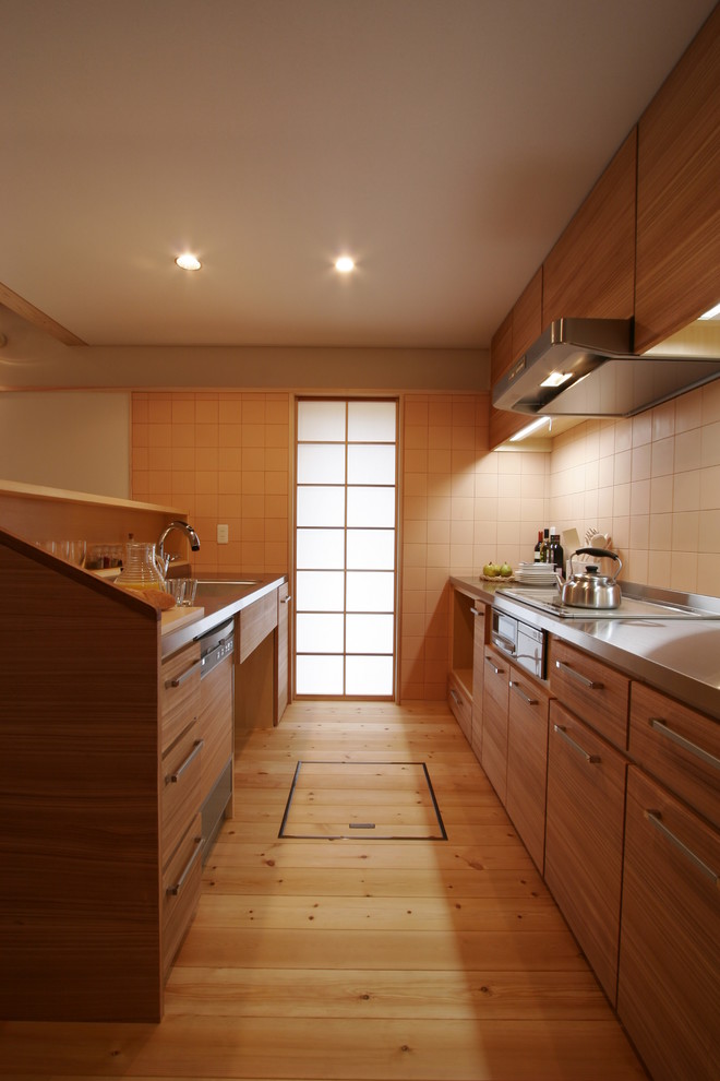 Bild på ett orientaliskt kök, med en integrerad diskho, skåp i mellenmörkt trä, bänkskiva i rostfritt stål, beige stänkskydd, stänkskydd i trä, rostfria vitvaror, mellanmörkt trägolv, beiget golv, släta luckor och en köksö