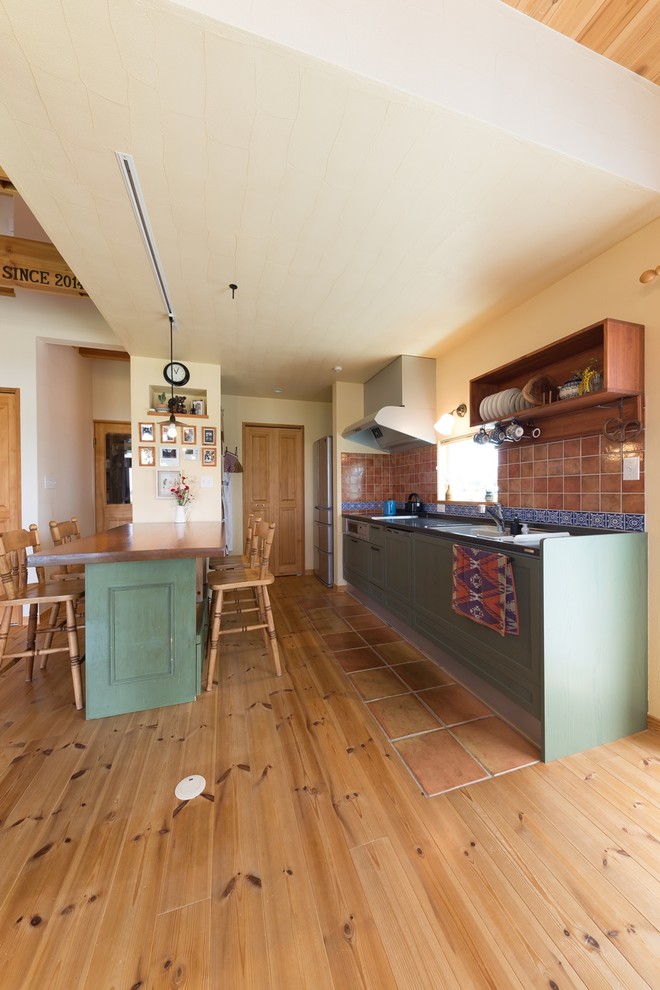 На фото: прямая кухня-гостиная в восточном стиле с одинарной мойкой, фасадами с утопленной филенкой, зелеными фасадами, коричневым фартуком, полом из терракотовой плитки и коричневым полом