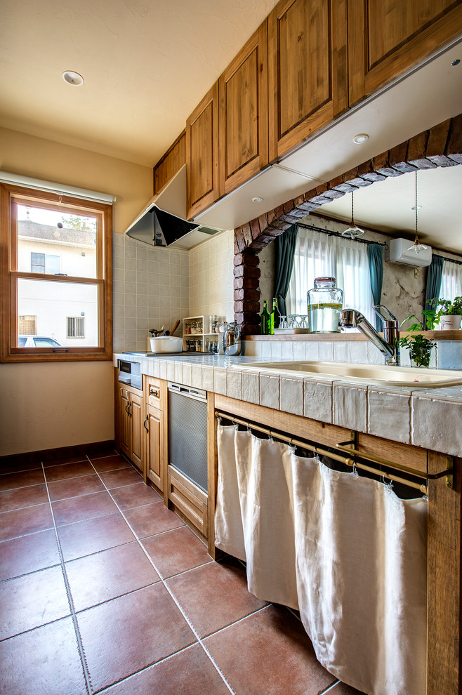 他の地域にある地中海スタイルのおしゃれなキッチン (ドロップインシンク、落し込みパネル扉のキャビネット、中間色木目調キャビネット、テラコッタタイルの床、茶色い床) の写真