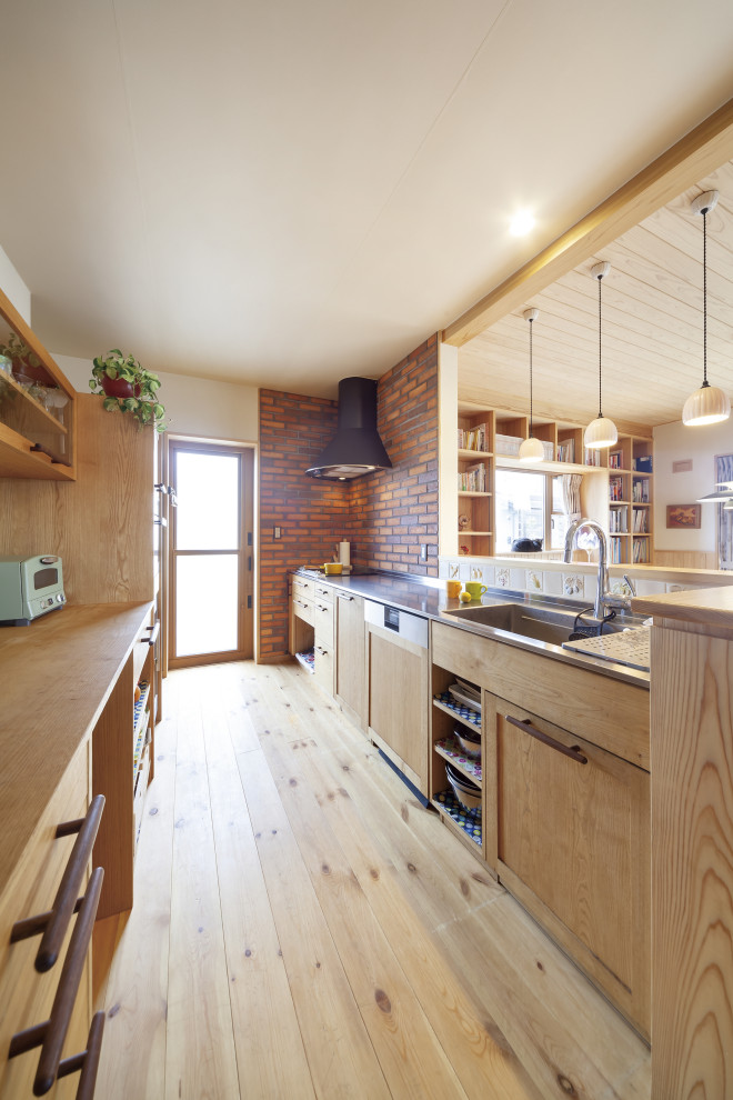 Idéer för att renovera ett stort brun linjärt brunt kök med öppen planlösning, med en integrerad diskho, skåp i shakerstil, skåp i ljust trä, bänkskiva i rostfritt stål, brunt stänkskydd, stänkskydd i tegel, rostfria vitvaror, ljust trägolv och beiget golv