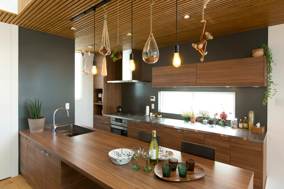 Exempel på ett lantligt kök, med en undermonterad diskho, släta luckor, skåp i mellenmörkt trä, bänkskiva i rostfritt stål, brunt stänkskydd, rostfria vitvaror, ljust trägolv och en halv köksö