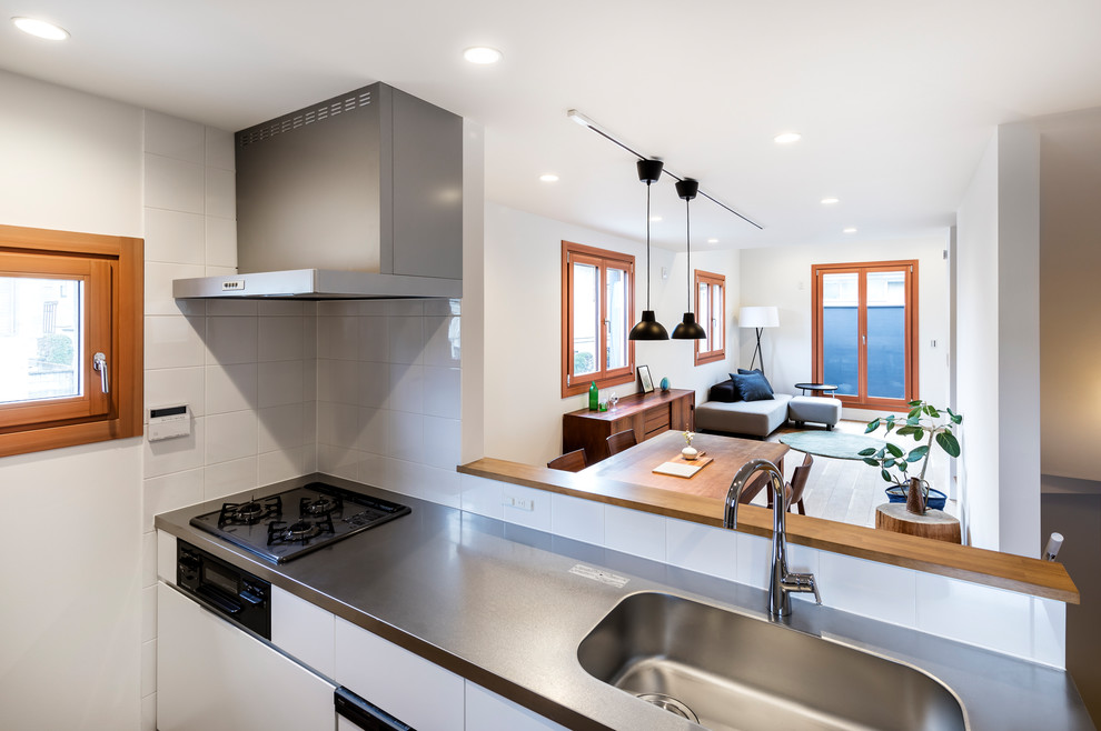 Idéer för ett mellanstort modernt linjärt kök med öppen planlösning, med en undermonterad diskho, bänkskiva i rostfritt stål, vitt stänkskydd, stänkskydd i glaskakel, vita vitvaror, mellanmörkt trägolv och brunt golv